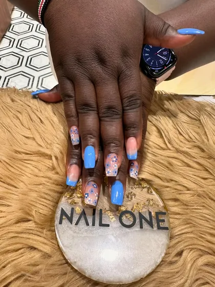 A close-up of the blue-tipped nails, highlighting the delicate floral art and sparkling glitter on the accent nails.