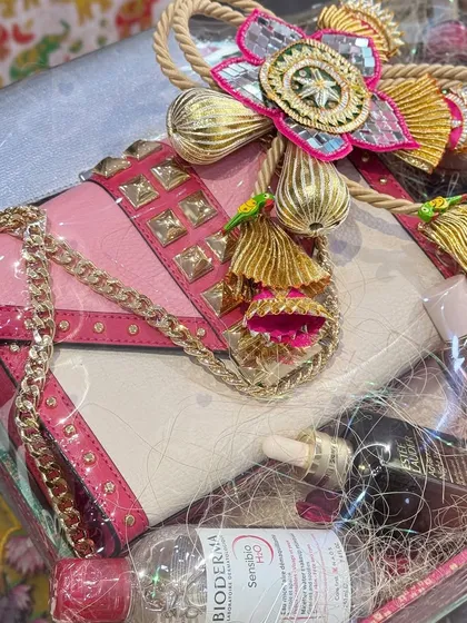 A closer look at a luxury trousseau hamper. This gift includes a stylish handbag and premium skincare products, all beautifully packaged with traditional Indian 'latkans' for a festive touch.