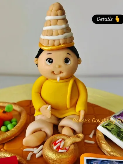 A close-up of the handcrafted fondant baby topper for the Annaprashan cake, showing the detailed work on the traditional Bengali 'topor' and the symbolic items surrounding him.