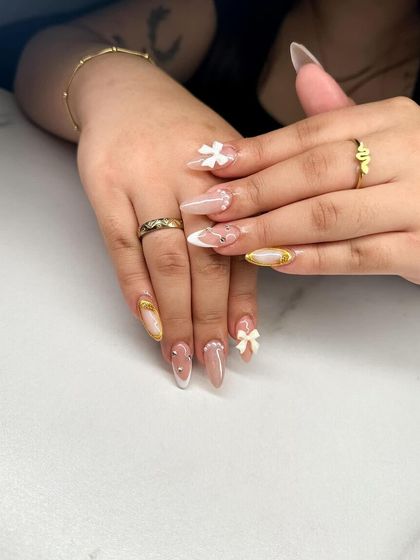 A beautiful and intricate design featuring a nude base, white French tips, and delicate 3D white bows with gold accents.
