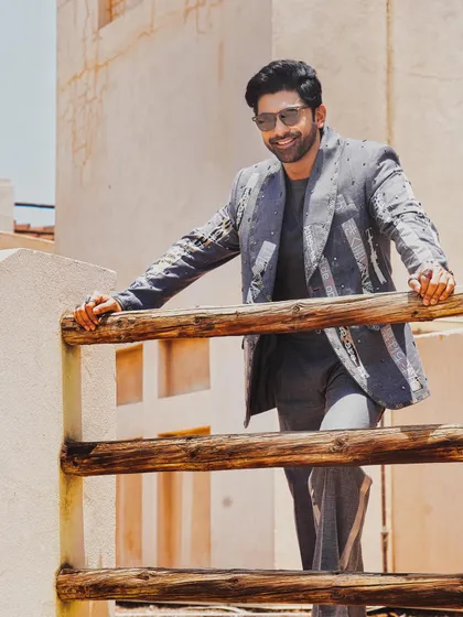 Taaha Shah wears the Paradox Suit, a grey jacket defined by its abstract prints, contrasting patches, and metal stud details. It's a piece for those who appreciate avant-garde design and meticulous craftsmanship.