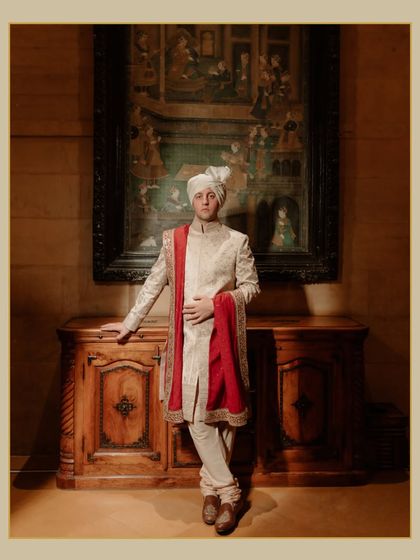 A classic portrait of the groom at his Suryagarh wedding. He stands against a backdrop of traditional art and antique furniture, exuding timeless elegance.