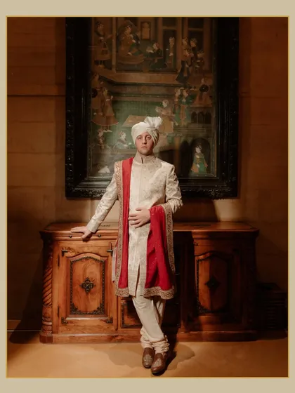 A classic portrait of the groom at his Suryagarh wedding. He stands against a backdrop of traditional art and antique furniture, exuding timeless elegance.