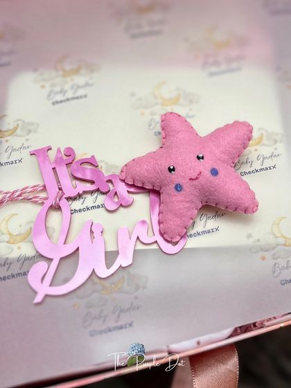 A close-up of the "It's a Girl" acrylic tag and a sweet felt star, details that add a personal and handmade touch to the celestial-themed gift.