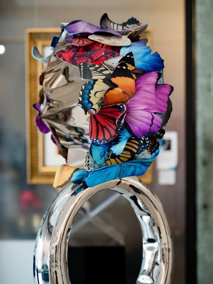 A close-up of the "Flight to Infinity" sculpture, focusing on the vibrant butterfly motifs that seem to grow out of the polished metal ring.