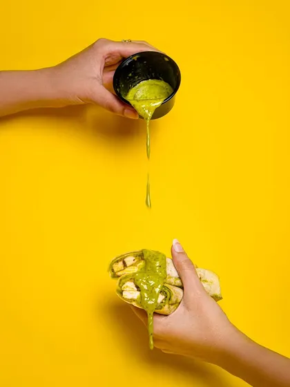 A dynamic shot of green chutney being poured over a snack. The bright yellow background and sense of motion make this a very engaging image.