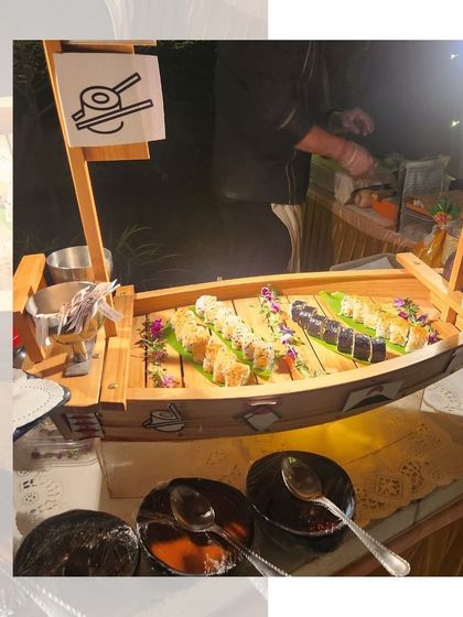 A live sushi counter in action. Our chef is seen preparing fresh sushi rolls on a traditional bamboo boat, providing both entertainment and delicious food for guests.