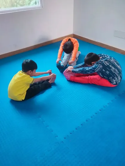Three young students practice their forward bend stretches together. Group activities help build camaraderie and motivate them to push each other.