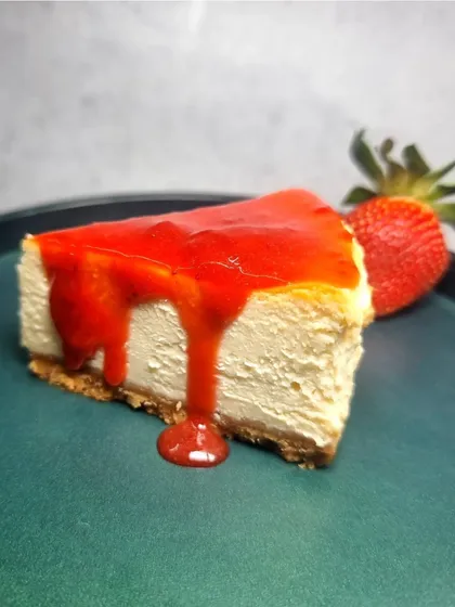 A slice of our NYC-Style Cheesecake generously drizzled with a vibrant strawberry sauce. It's a perfect combination of creamy, sweet, and fruity.