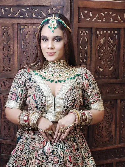 A full look of a model wearing a multi-coloured printed lehenga with a heavy Kundan and green bead jewellery set.