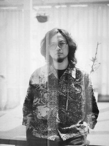 A black and white portrait of musician Taba Chake, with reflections creating a double-exposure effect. It adds a dreamy, artistic layer to the image.