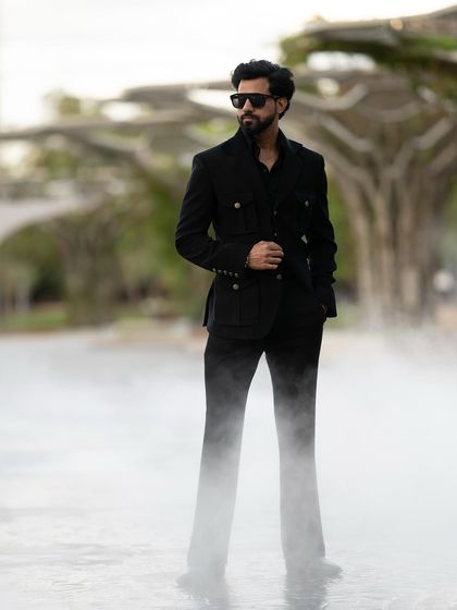 The dramatic, misty setting adds an element of mystery and intrigue, perfectly complementing the all-black, sophisticated ensemble.