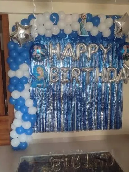A 'Frozen' themed birthday party at home with a blue shimmer curtain and balloon garland.