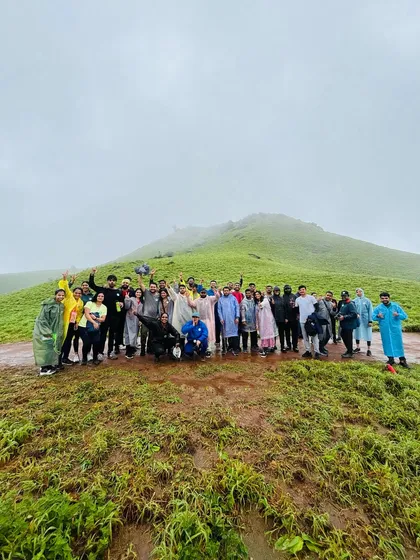 A large group of adventurers spread out across a wet, green meadow during a monsoon trek to Bandaje.