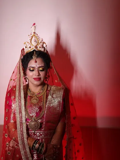 A dramatic portrait of a Bengali bride. The traditional 'mukut' and the intricate designs on her forehead are the centerpieces of this look, enhanced by makeup that highlights her eyes and features.