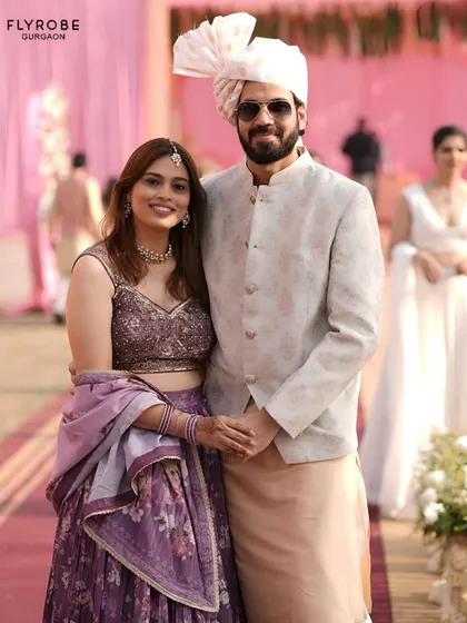 Why buy when you can rent luxury? This couple looks effortlessly stylish in their coordinated purple floral lehenga and off-white sherwani.