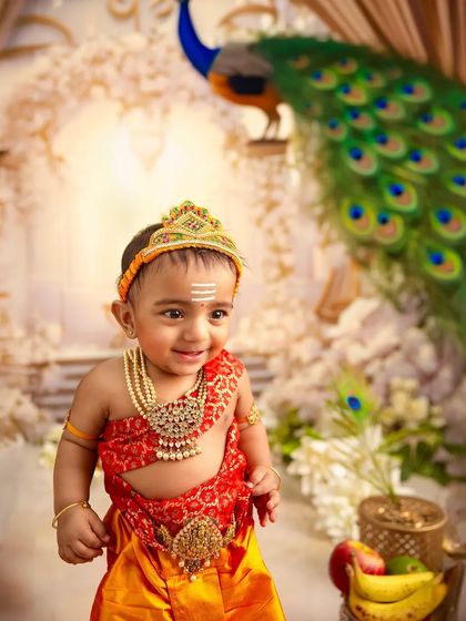 A smile from a little god. This close-up shot captures the joyful expression of the baby dressed as Karthikeya, highlighting the detailed costume and jewelry.