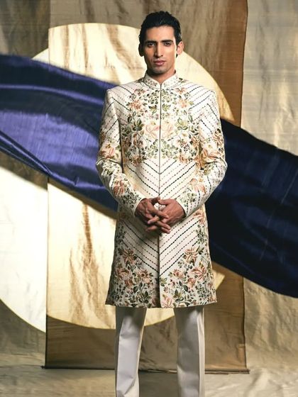 This elegant white sherwani features delicate floral and vine embroidery, offering a sophisticated and charming look for the modern groom.