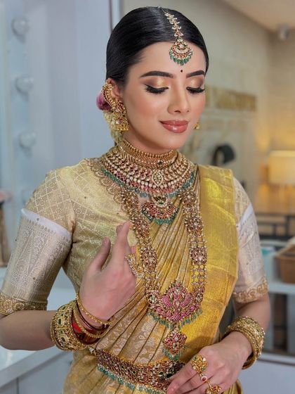A beautiful bride in a golden Kanjeevaram saree. The makeup features a soft gold shimmer on the eyes and a glossy nude lip for a modern yet traditional look.