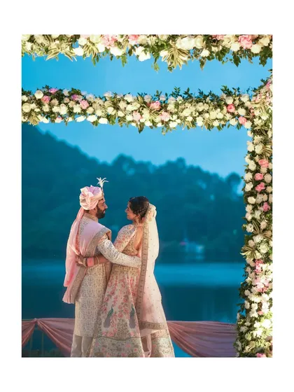 A stunning portrait of the couple under a floral arch against a serene lake at dusk.