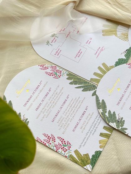 Arched itinerary cards with a vellum overlay showing a map of the venue. The design uses the same tropical illustrations as the main invitations, ensuring a cohesive look.