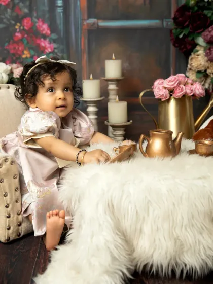 A thoughtful look during her elegant tea party session. The rich floral backdrop and soft lighting create a beautiful, painterly effect.