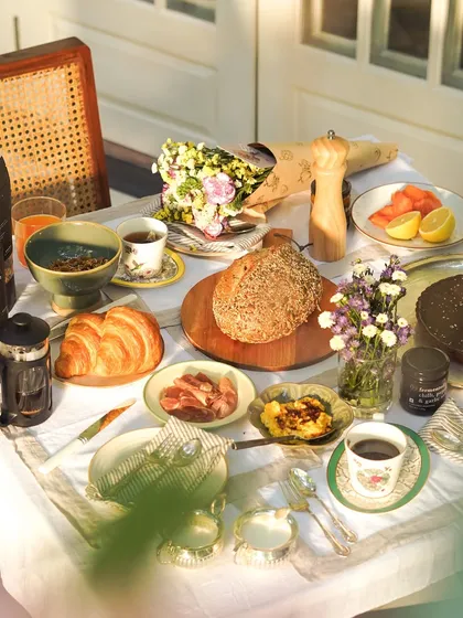 A beautiful brunch spread for Mother's Day, showcasing how our delivery items can create a full celebratory meal at home. The table features our seeded bread, croissants, coffee, and a chocolate tart.