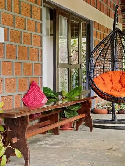 A relaxing spot on the veranda of Villa Magnolia, with a swing chair and a rustic wooden bench. The exposed laterite brick wall adds texture and a sense of place.