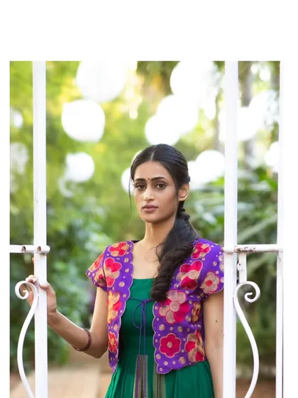 A stunning jade green dress made from traditional silk with a zari border, paired with a vibrant violet hand-embroidered jacket for a bold, contemporary look.