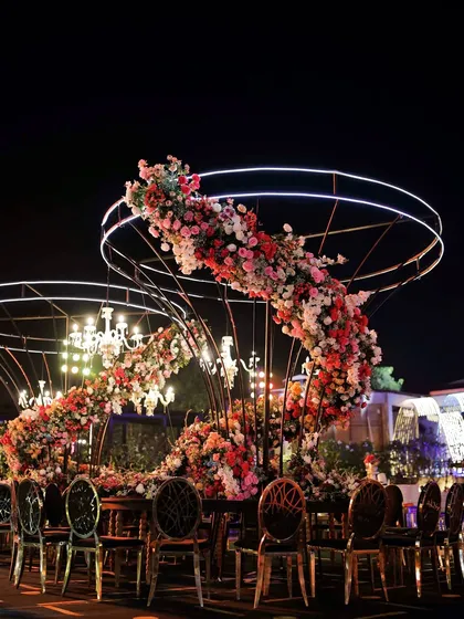 A breathtaking floral spiral centerpiece designed for a Sangeet night, where modern structure meets classic romance. This custom installation, illuminated by elegant chandeliers, creates an intimate yet grand dining experience under the stars.