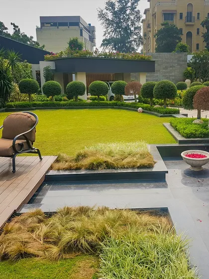A daytime view of a multi-level garden space, featuring a wooden deck, a water feature with decorative bowls, and meticulously manicured lawns and topiary. This design uses different levels and materials to create distinct functional zones.