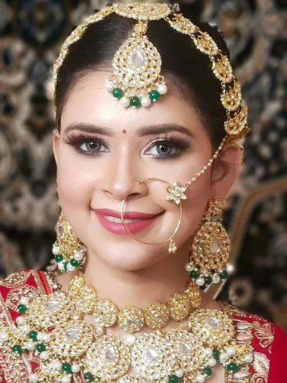 A happy bride smiling in a full Pachi Kundan set with green bead accents. This set includes a choker, matching earrings, maang tikka, and a simple, elegant nath.