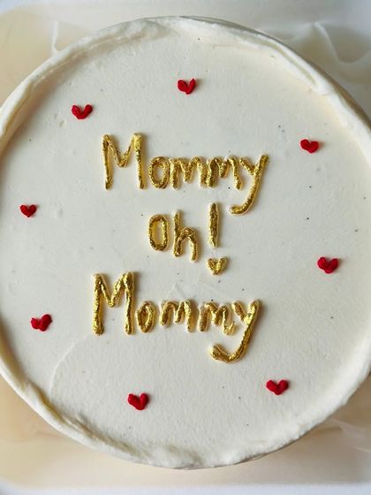 A simple and elegant Mother's Day bento cake. The white buttercream is adorned with "Mommy Oh! Mommy" in gold lettering and tiny red hearts, perfect for showing your love.