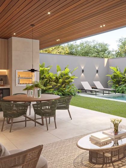A poolside patio designed for entertaining. The space includes a dining area and an outdoor kitchen with a built-in grill, all under a covered ceiling and surrounded by lush tropical plants for privacy.