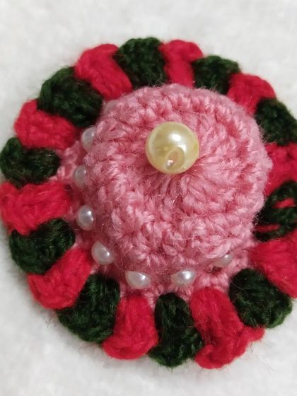 A close-up of the matching cap for the red flower dress. It features a pink base with red and green accents and a large pearl in the center.