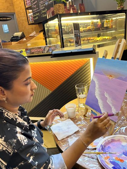 A participant fully engaged in painting her abstract beach scene, with a palette of pastel colors beside her.