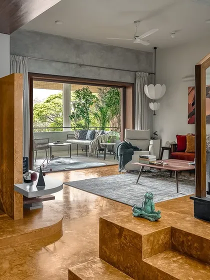 Bold choices can define a home. The vibrant turmeric-yellow oxide flooring brings immense warmth to this space, beautifully contrasting with the cool grey tones and connecting the multi-level living areas to the lush green balcony outside.