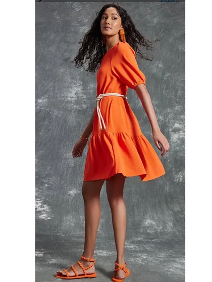 A bright and cheerful orange tiered dress styled for a summer collection. The movement of the dress and matching accessories create a fun, energetic vibe.