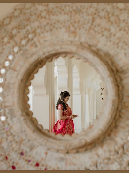 A creative portrait of the bride seen through a circular mirror. This unique framing adds an artistic touch to her Haldi day look in Udaipur.