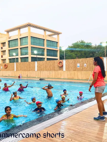 A group of young swimmers participates in a guided lesson during our summer camp. An instructor leads the session from the poolside, demonstrating our structured approach to teaching swimming techniques in a group setting.