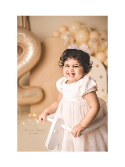 A close-up of a happy two-year-old girl on her rocking horse, with soft lights in the background.