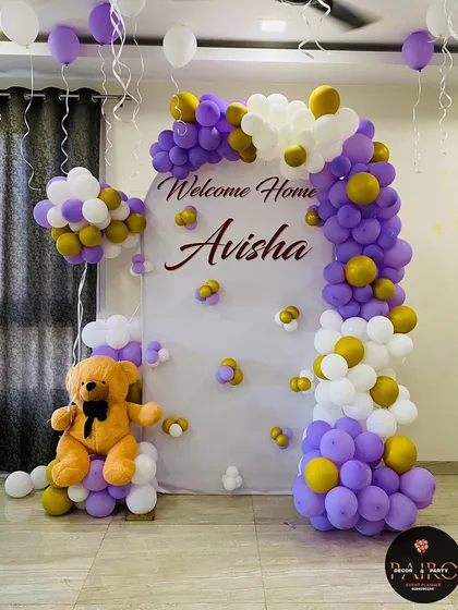 Welcome home decorations can be both grand and personal. For baby Avisha's arrival, I created this elegant backdrop with a custom name sign, a purple, white, and gold balloon arch, and a cute teddy bear prop, transforming the family's living room.