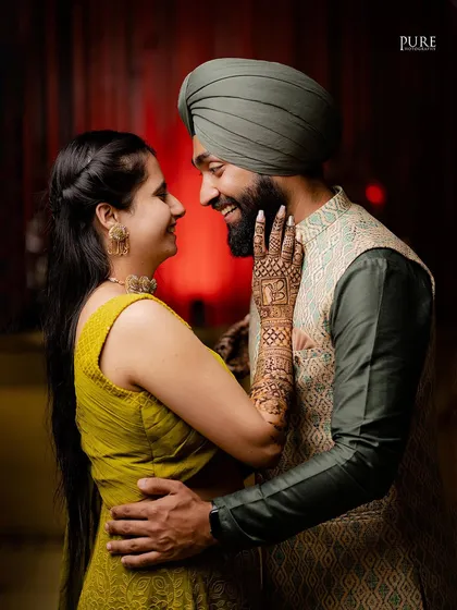 A playful and romantic moment where the bride touches the groom's face with her henna-adorned hand.
