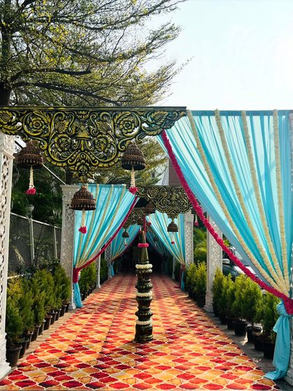 A full view of the traditional walkway, where light blue and pink drapes are complemented by hanging temple bells and ornate pillars. This entrance is a beautiful fusion of color and culture.