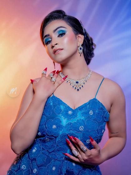 A creative shot featuring a model in a blue gown with intricate nail art and a sparkling diamond and sapphire necklace.