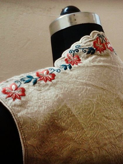 A detail shot of the shoulder and high-neck collar of a custom shrug. The design features a scalloped edge and colorful floral embroidery, showcasing the fine finishing of my garments.