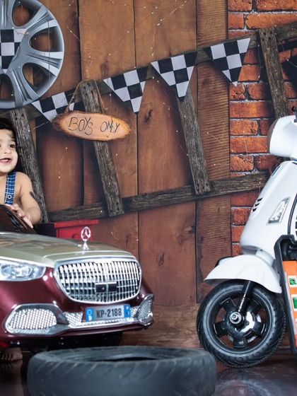 A joyful moment in the garage. This little mechanic is all smiles as he pretends to drive his car, surrounded by tools and a cool white scooter.