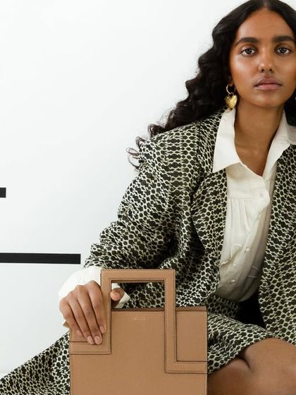 A more direct, seated pose from the same campaign. This provides a clear and elegant view of the handbag, styled with a chic printed suit.