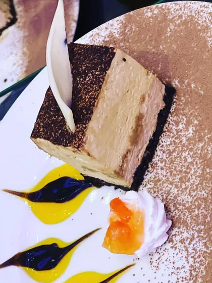 A beautifully plated tiramisu slice, dusted with cocoa powder and garnished with white chocolate. This classic Italian dessert is a testament to my expertise in Western and fusion bakery.