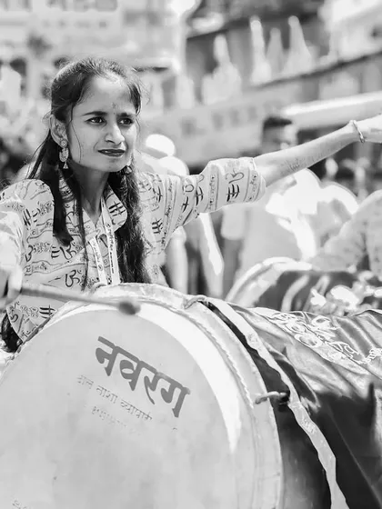 A black and white portrait of a female dhol player with a focused expression.